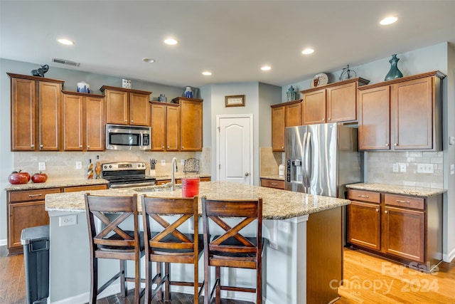 kitchen featuring a kitchen breakfast bar, tasteful backsplash, stainless steel appliances, a kitchen island with sink, and light hardwood / wood-style flooring