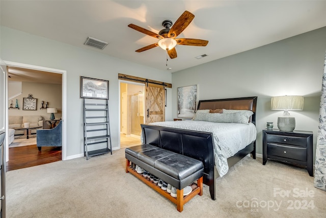 carpeted bedroom featuring a barn door, ceiling fan, and ensuite bath