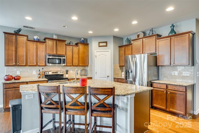 kitchen with a breakfast bar, brown cabinetry, visible vents, and stainless steel appliances