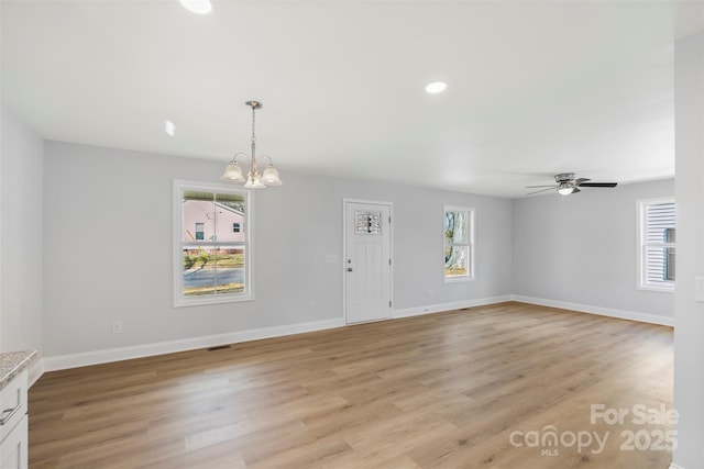 unfurnished living room featuring a healthy amount of sunlight, ceiling fan with notable chandelier, and light wood-type flooring