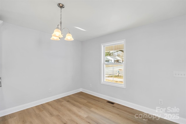 empty room with light hardwood / wood-style flooring and a chandelier