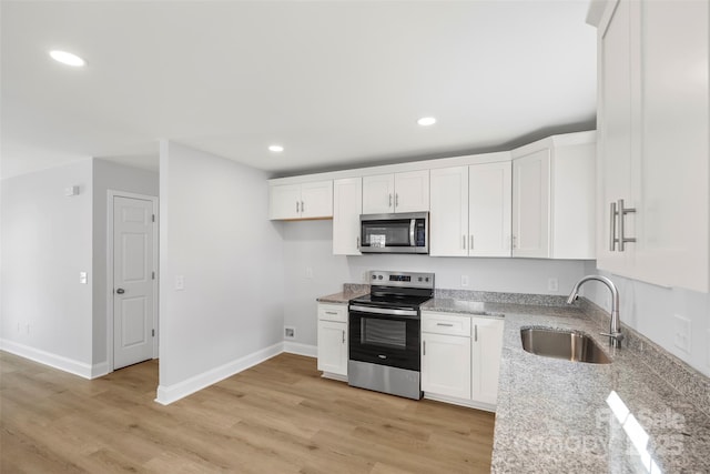 kitchen with appliances with stainless steel finishes, white cabinetry, sink, light stone counters, and light hardwood / wood-style floors