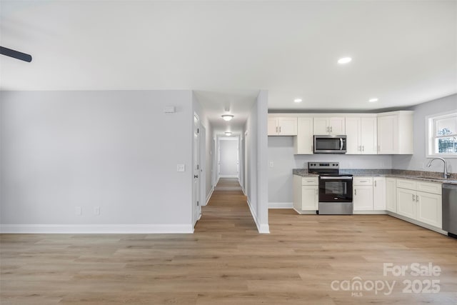 kitchen with sink, white cabinetry, stainless steel appliances, stone countertops, and light wood-type flooring