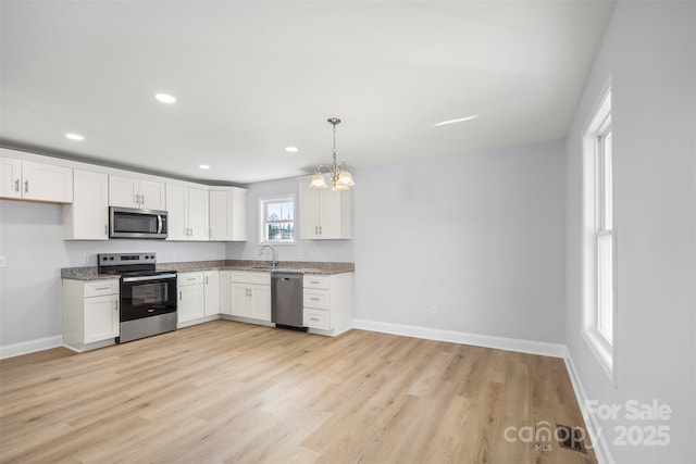 kitchen with appliances with stainless steel finishes, white cabinetry, sink, hanging light fixtures, and light wood-type flooring