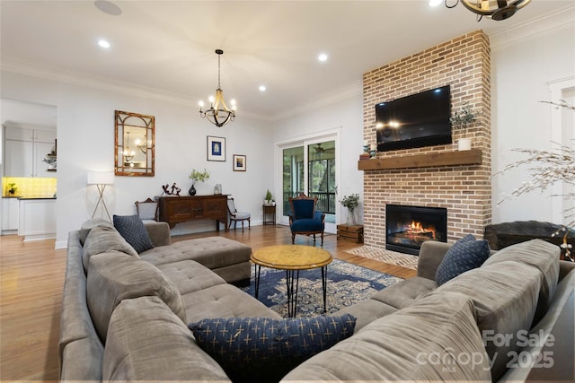 living room featuring hardwood / wood-style flooring, ornamental molding, a brick fireplace, and a chandelier