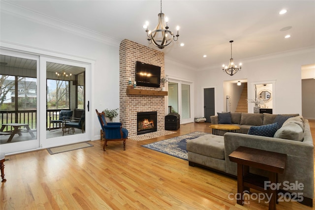 living room with ornamental molding, a chandelier, a brick fireplace, and light wood-type flooring