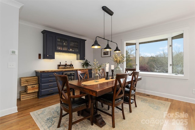 dining area with crown molding, light hardwood / wood-style floors, and indoor bar