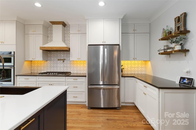 kitchen featuring appliances with stainless steel finishes, tasteful backsplash, light hardwood / wood-style floors, custom range hood, and white cabinets