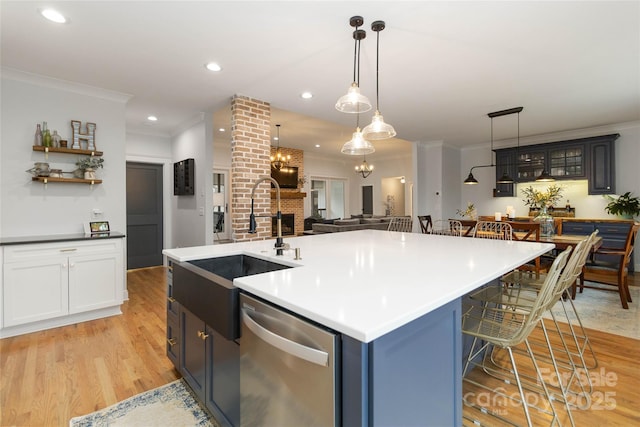 kitchen with a breakfast bar, dishwasher, an island with sink, light hardwood / wood-style floors, and a brick fireplace