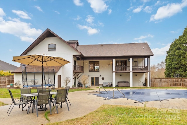 back of house featuring a swimming pool with hot tub, a trampoline, a patio, and a balcony