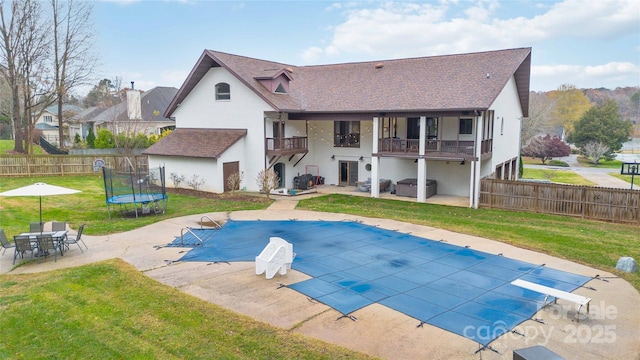 rear view of house featuring a balcony, a covered pool, a trampoline, and a lawn