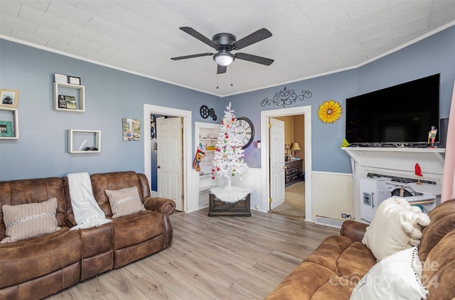 living room featuring crown molding, wooden walls, ceiling fan, and light wood-type flooring