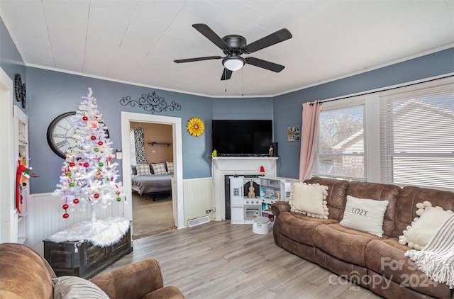 living room featuring light wood-type flooring, wooden walls, ceiling fan, and crown molding