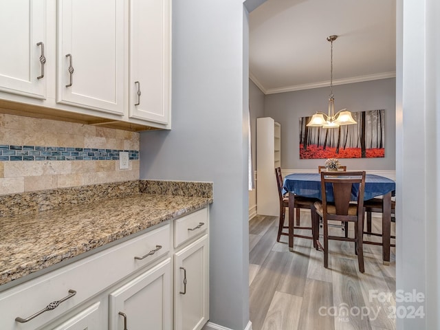 kitchen featuring light stone countertops, crown molding, white cabinets, and light wood-type flooring