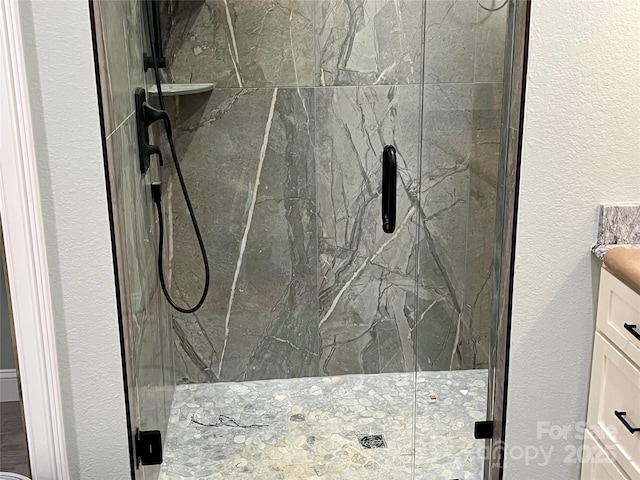 bathroom with a marble finish shower, vanity, and a textured wall