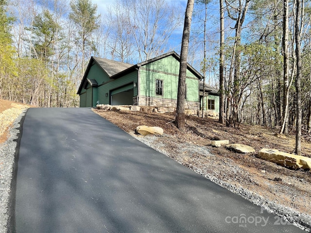 view of property exterior with stone siding, asphalt driveway, and a garage