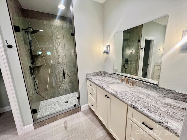bathroom featuring a marble finish shower, vanity, baseboards, and wood finished floors