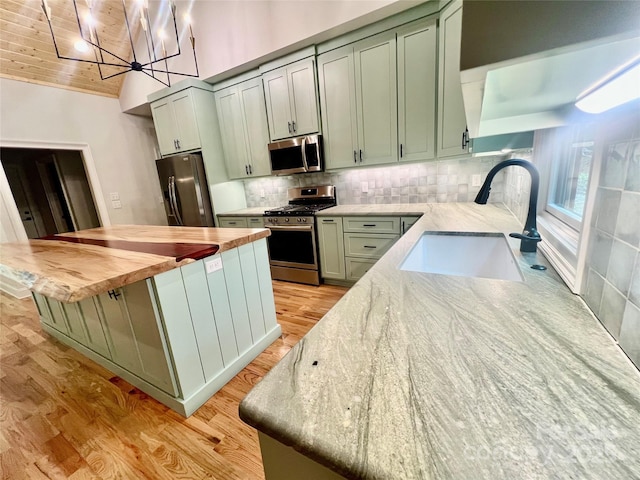 kitchen with stainless steel appliances, a sink, light wood finished floors, a center island, and butcher block countertops