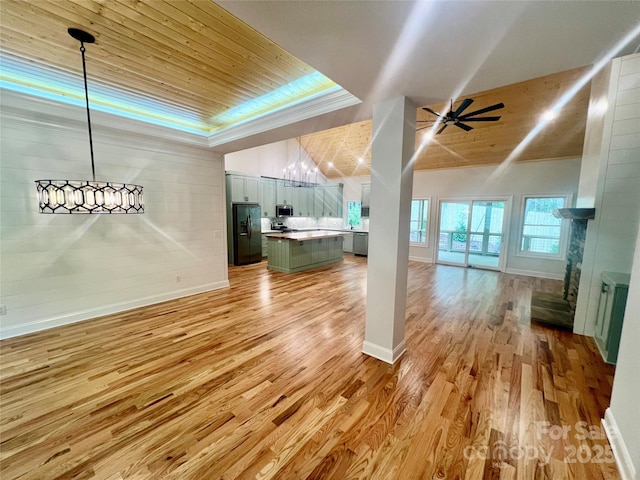 unfurnished living room featuring light wood-style flooring, a tray ceiling, wooden ceiling, baseboards, and a ceiling fan