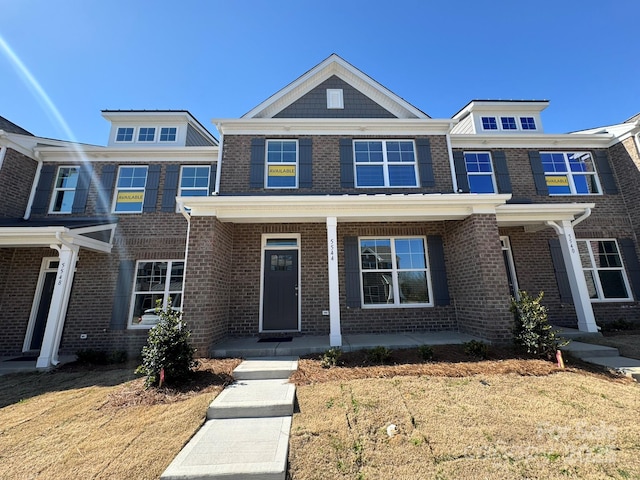 townhome / multi-family property featuring covered porch, a front lawn, and brick siding