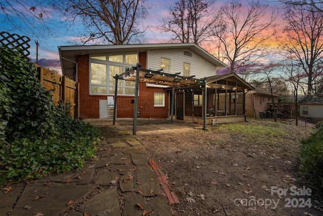 back house at dusk featuring a pergola, a patio, and a sunroom