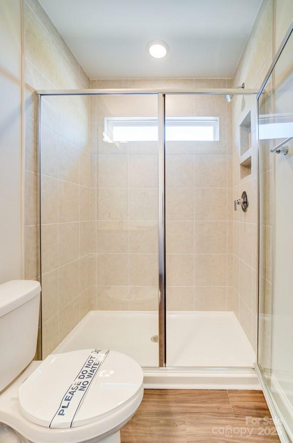 full bathroom with toilet, a stall shower, and wood finished floors