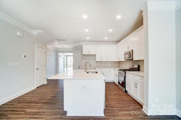 kitchen featuring an island with sink, crown molding, backsplash, a sink, and stainless steel appliances