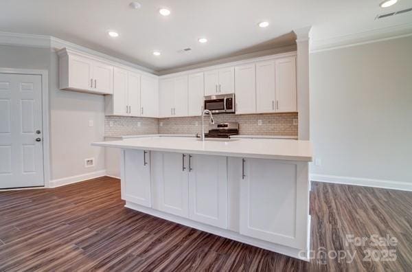 kitchen with dark wood finished floors, white cabinetry, crown molding, and appliances with stainless steel finishes