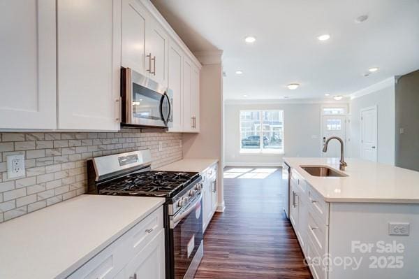 kitchen with light countertops, stainless steel appliances, dark wood finished floors, a sink, and an island with sink