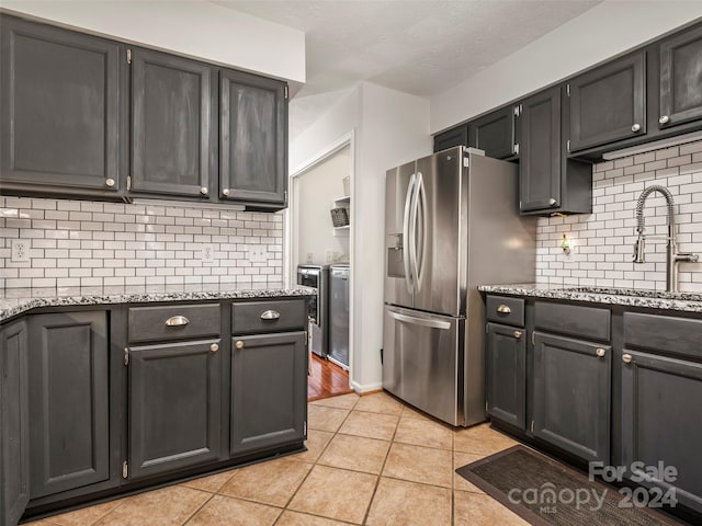 kitchen with light stone countertops, sink, stainless steel fridge, decorative backsplash, and washer and clothes dryer