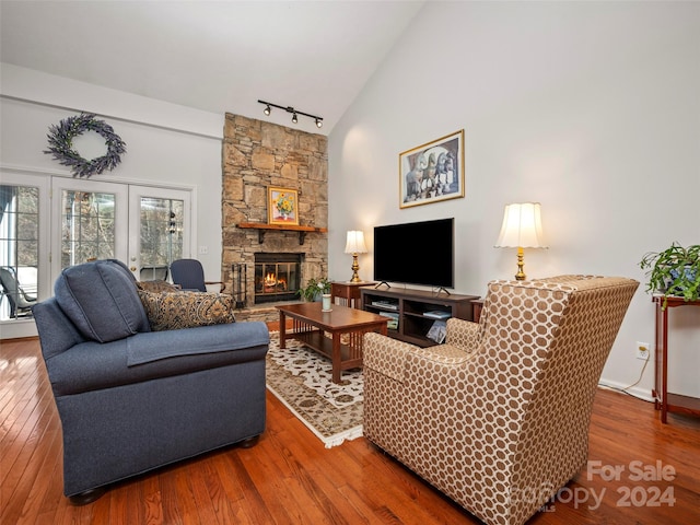 living room with hardwood / wood-style floors, high vaulted ceiling, track lighting, and a stone fireplace