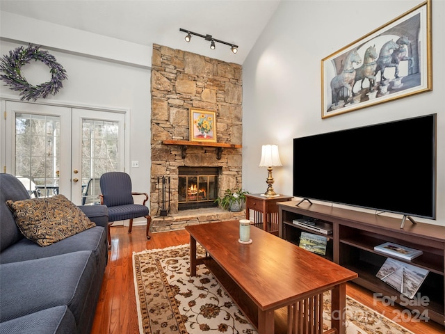 living room featuring french doors, rail lighting, vaulted ceiling, hardwood / wood-style flooring, and a stone fireplace