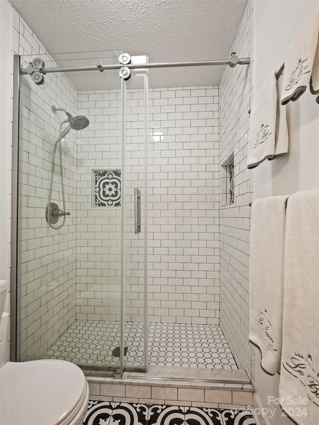 bathroom with a textured ceiling, toilet, and a shower with door