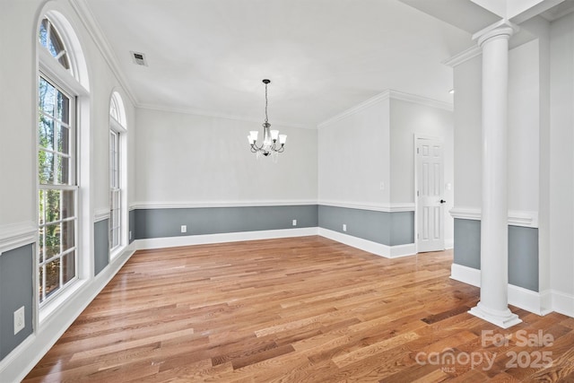 empty room with ornamental molding, light wood-type flooring, a notable chandelier, and decorative columns