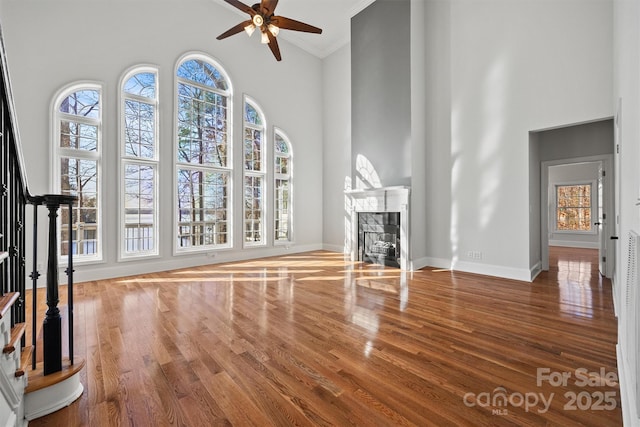 unfurnished living room featuring a towering ceiling, a fireplace, ceiling fan, and crown molding