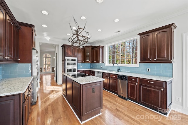 kitchen with appliances with stainless steel finishes, light wood-type flooring, crown molding, a kitchen island, and sink