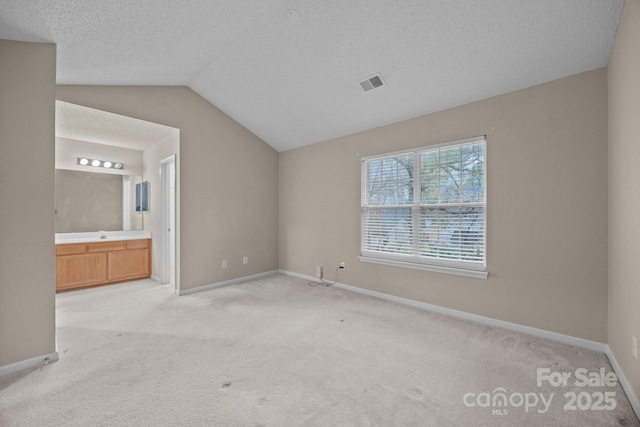 unfurnished bedroom featuring connected bathroom, vaulted ceiling, light carpet, and a textured ceiling