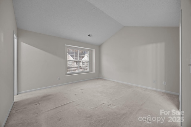 empty room featuring light colored carpet, vaulted ceiling, and a textured ceiling