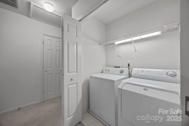 clothes washing area featuring separate washer and dryer, light colored carpet, and a textured ceiling