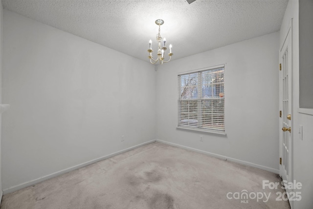 carpeted empty room featuring a textured ceiling and a notable chandelier