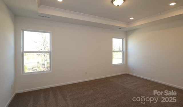 unfurnished room with a raised ceiling, crown molding, and dark colored carpet