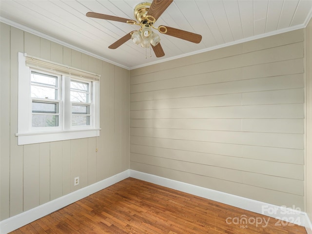 empty room featuring hardwood / wood-style flooring, ceiling fan, crown molding, and wood walls