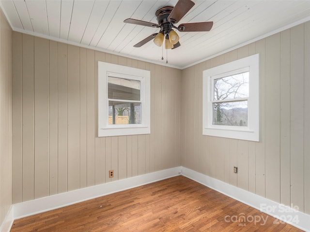 empty room featuring hardwood / wood-style floors, ceiling fan, ornamental molding, and wood walls