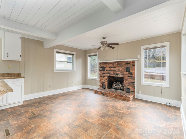 unfurnished living room with beamed ceiling, ceiling fan, a wealth of natural light, and a brick fireplace