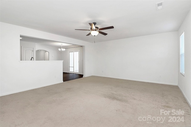 carpeted spare room featuring ceiling fan with notable chandelier