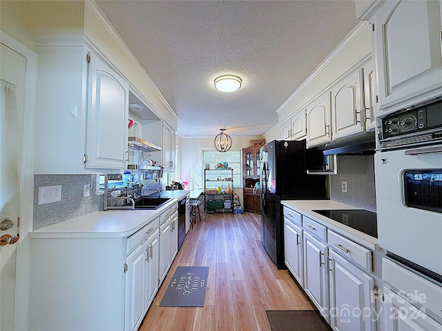 kitchen with light wood-type flooring, ornamental molding, a textured ceiling, black appliances, and white cabinetry