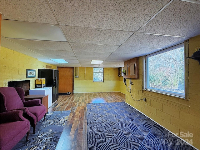 basement featuring hardwood / wood-style floors, black fridge, and a drop ceiling