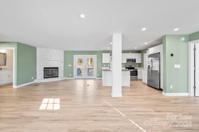 unfurnished living room with a large fireplace, light hardwood / wood-style flooring, and french doors