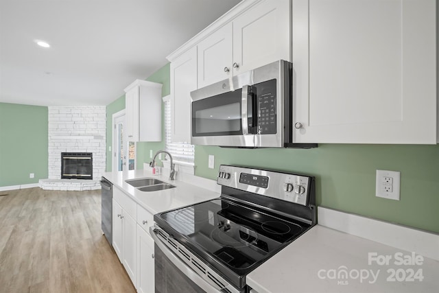 kitchen with light wood-type flooring, stainless steel appliances, sink, white cabinets, and a stone fireplace