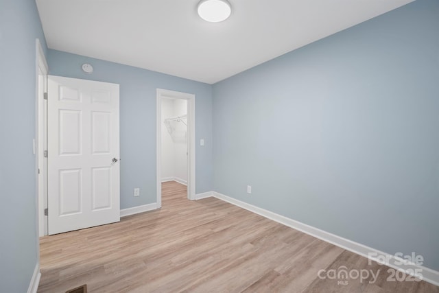 unfurnished bedroom featuring a walk in closet, light wood-type flooring, and a closet